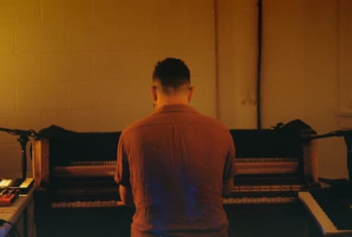 Nathan Shubert at an upright piano, seen from behind
